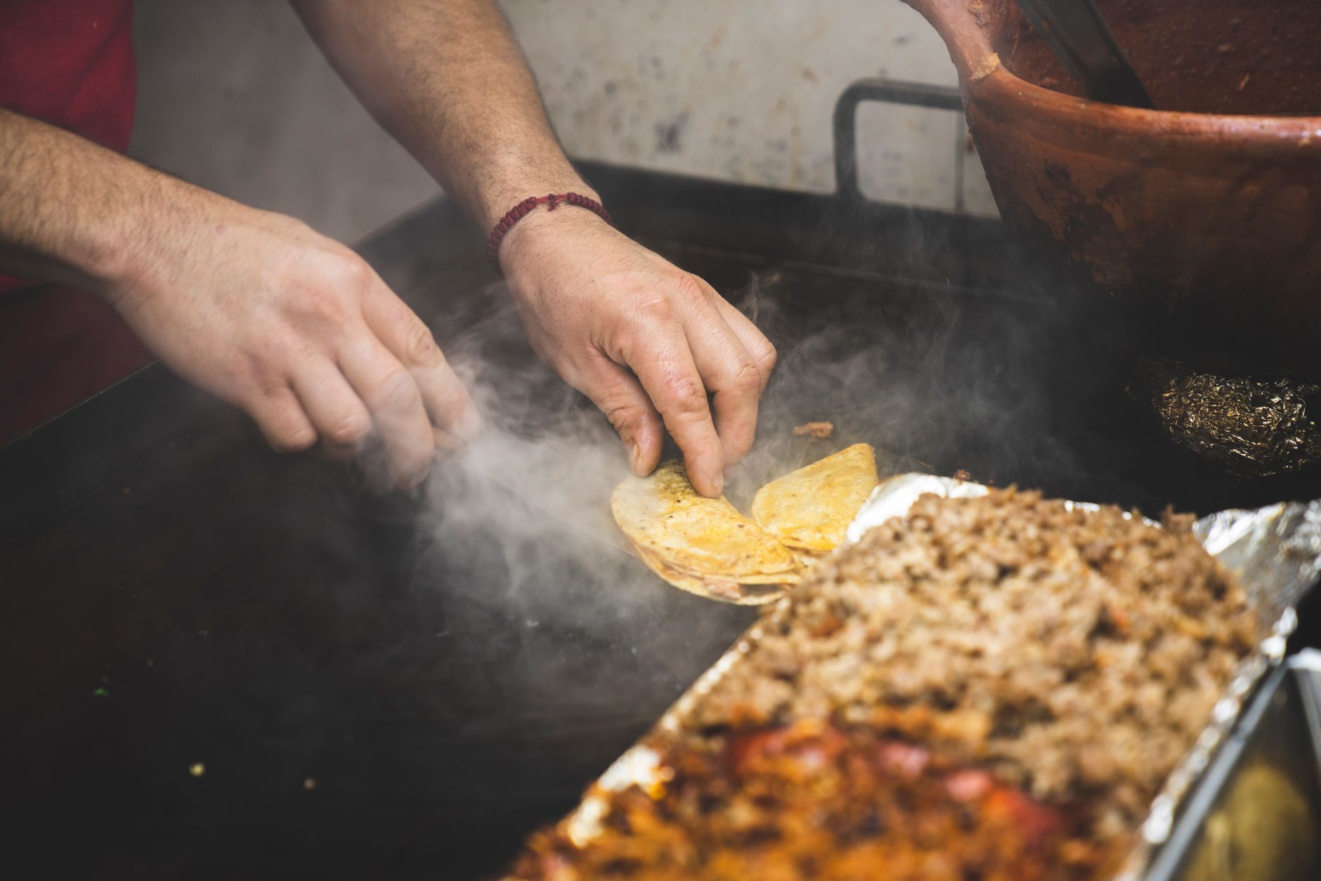 Manos de un taquero preparando tacos al vapor sobre el comal de un puesto callejero