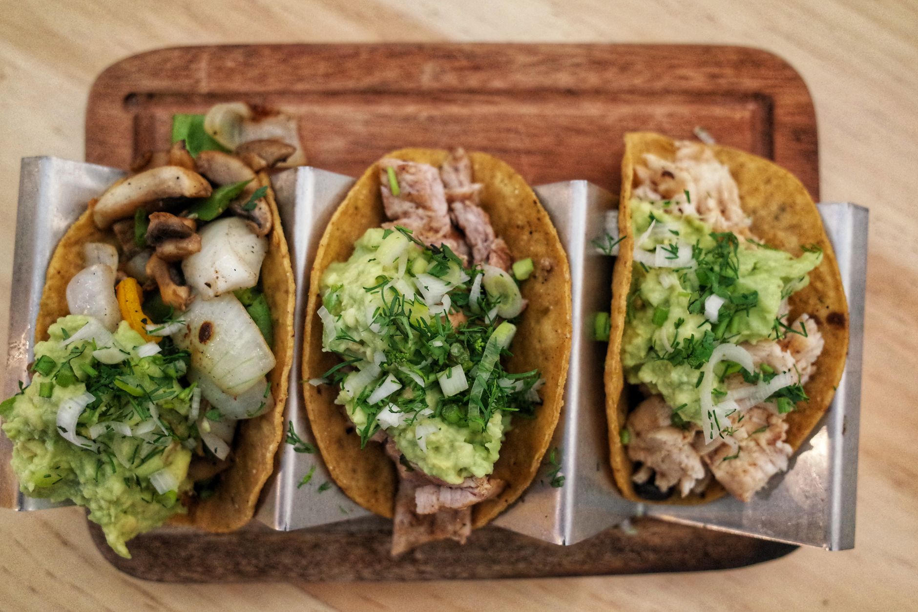 Tacos recién preparados con guacamole sobre una tabla de madera, listos para servir